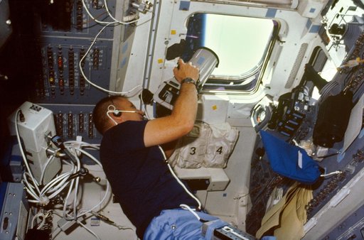 Astronaut Robert Overmyer aims Linhof camera through flight deck windows