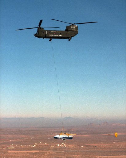 With a small stabilization parachute trailing behind, the X-40 sub-scale technology demonstrator is suspended under a U.S. Army CH-47 Chinook cargo helicopter during a captive-carry test flight