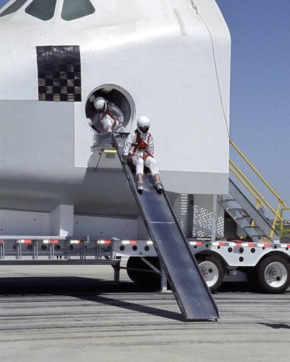 A volunteer "astronaut" starts down an exit slide from a Space Shuttle crew compartment mockup during a rescue and recovery training exercise