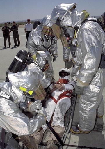 Clad in thermal protection suits, fire-rescue crews strap a stand-in "astronaut" into a litter during a Space Shuttle rescue training exercise at Edwards AFB