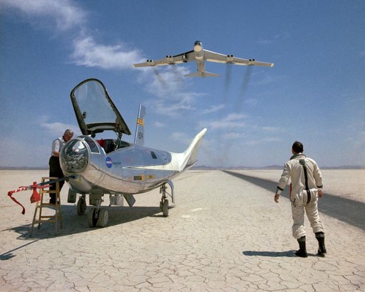 NASA research pilot Bill Dana takes a moment to watch NASA's NB-52B cruise overhead after a research flight in the HL-10. On the left, John Reeves can be seen at the cockpit of the lifting body