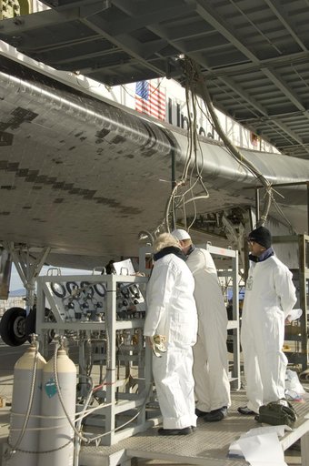 Technicians in protective coveralls check pressures of fluid systems during deservicing operations on Space Shuttle Endeavour after its landing at Edwards AFB