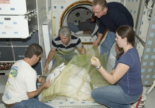 United Space Alliance technicians wrap the lower portion of an Extravehicular Mobility Unit (EMU) spacesuit prior to removal from Space Shuttle Endeavour