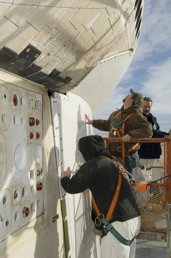 Technicians fasten down the flanges of the aerodynamic tail cone after installation on NASA's Space Shuttle Endeavour prior to its ferry flight back to Florida