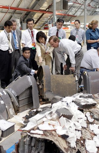 KENNEDY SPACE CENTER, FLA. -  On a KSC visit, Executive Director of NASDA Koji Yamamoto (kneeling, left) reaches out to a piece of Columbia debris in the Columbia Debris Hangar.  At right is Shuttle Launch Director Mike Leinbach, who is explaining recovery and reconstruction efforts.  Mr. Yamamoto i