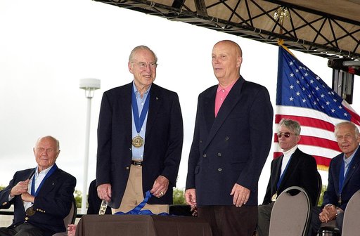 KENNEDY SPACE CENTER, FLA. -  At the KSC Visitor Complex, former astronaut James A. Lovell (standing left) greets former astronaut Story Musgrave (standing right) at his induction ceremony into the U.S. Astronaut Hall of Fame. Also seated on the dais are, from left, former astronaut and Senator John