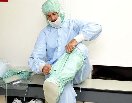 KENNEDY SPACE CENTER, FLA. -  A KSC employee dons the foot and leg covers of a "bunny suit," part of standard clean room apparel, before entering a clean room. The apparel is designed to cover the hair, clothing and shoes of employees to prevent particulate matter from contaminating the space flight