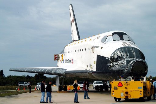 KENNEDY SPACE CENTER, FLA. -- After Endeavour’s rollout from inside the Orbiter Processing Facility, the transporter (foreground) prepares to tow it to the Vehicle Assembly Building for temporary transfer.  A protective cover surrounds the nose of Endeavour.  The move to the VAB allows work to be pe