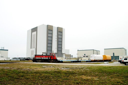 KENNEDY SPACE CENTER, FLA. - Moving past the 525-foot-high Vehicle Assembly Building, the red NASA engine pulls several containers enclosing segments of a solid rocket booster being returned to Utah for testing.  The segments were part of the STS-114 stack.  It is the first time actual flight segmen