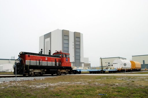 KENNEDY SPACE CENTER, FLA. - The red NASA engine moves forward past the Vehicle Assembly Building with its cargo of containers enclosing segments of a solid rocket booster being returned to Utah for testing.  The segments were part of the STS-114 stack.  It is the first time actual flight segments t