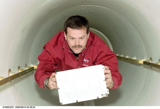 Pilot Altman carries a battery through the transfer tunnel during STS-106