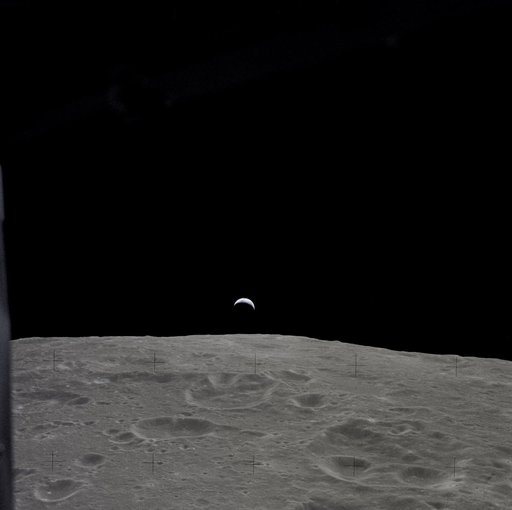 Earth rises above the lunar horizon as seen from Apollo 12 in lunar orbit