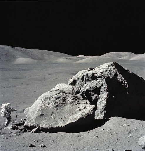Astronaut Harrison Schmitt standing next to boulder during third EVA