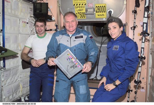 The Soyuz Taxi crew pose with the ISS ship log in Node 1 during Expedition Three