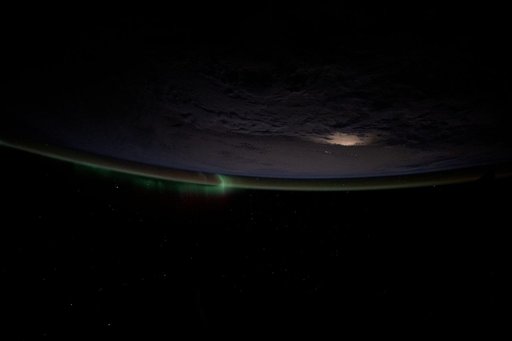 A wispy aurora intersects with Earth's atmospheric glow