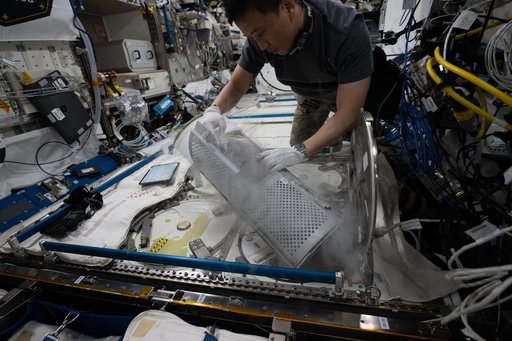 NASA astronaut Jonny Kim removes a cryogenic storage unit containing frozen protein crystal samples
