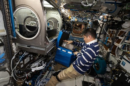 JAXA astronaut Takuya Onishi stows physics research hardware used during the Colloidal Solids experiment