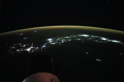 City lights trace the Japanese coastline underneath a dim yellow-green airglow