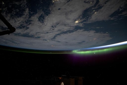 A wispy aurora caps Earth's horizon as an orbital sunrise illuminates the atmosphere