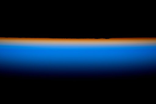 The last rays of an orbital sunset outline Earth’s horizon with a thin orange hue