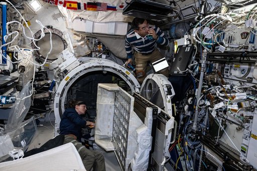 Astronauts Zena Cardman and Kimiya Yui remove a small satellite orbital deployer