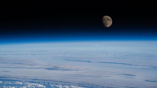 The waxing gibbous Moon rises above Earth’s blue atmosphere
