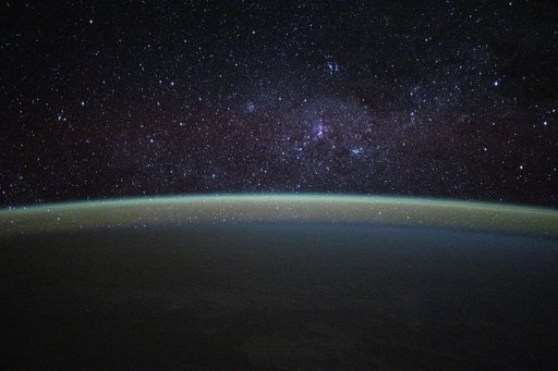 Stars fill the sky above a serene, blue-green airglow blanketing Earth's horizon