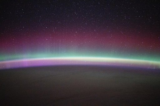 A green and red aurora australis shimmers beneath a starry sky