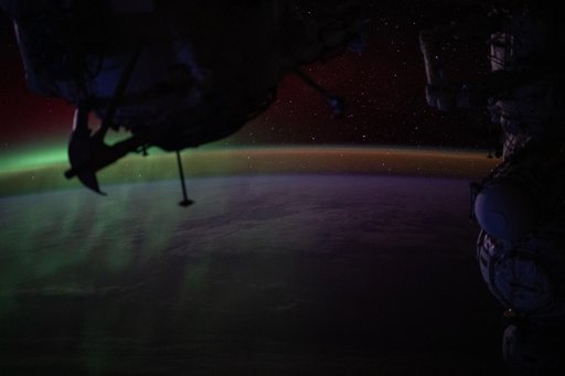 A wispy green aurora australis fades into a dim orange-yellow airglow above Earth’s horizon