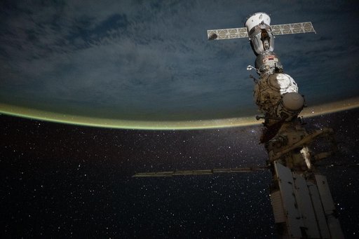 A yellow-green airglow blankets Earth’s horizon beneath a star-filled sky