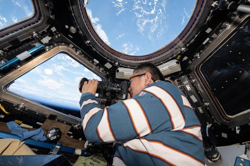 JAXA astronaut Kimiya Yui points a camera out a cupola window and photographs station hardware