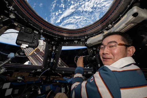 JAXA astronaut Kimiya Yui points a camera out a cupola window and photographs station hardware