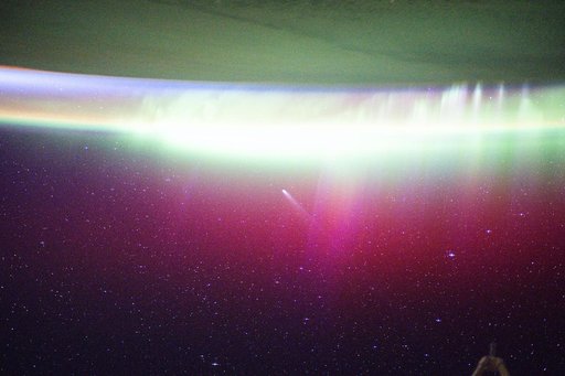 A bright, neon-like aurora radiates above Earth and seemingly absorbs Comet Lemmon