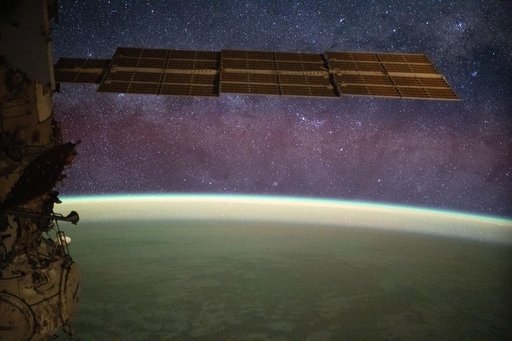 The Milky Way spans the night sky above a yellow-green airglow