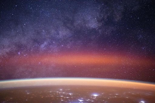 The Milky Way spans the night sky above a bright orange-yellow airglow
