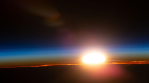 An orbital sunrise illuminates Earth's atmosphere and cloud tops