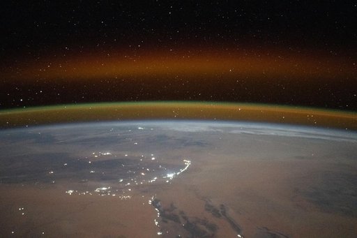 A yellow-red airglow blankets Earth's horizon above the Saharan landscape of Algeria