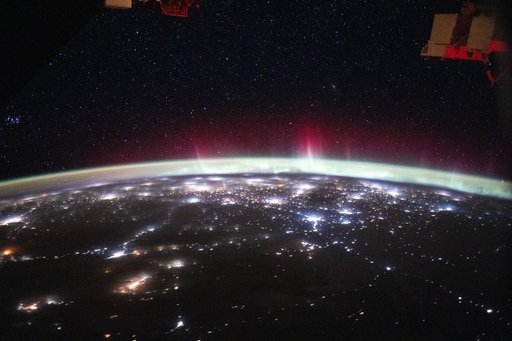An aurora streams above Earth’s atmospheric glow