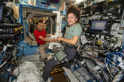 NASA astronauts Chris Williams and Jessica Meir inspect and configure a spacesuit jetpack
