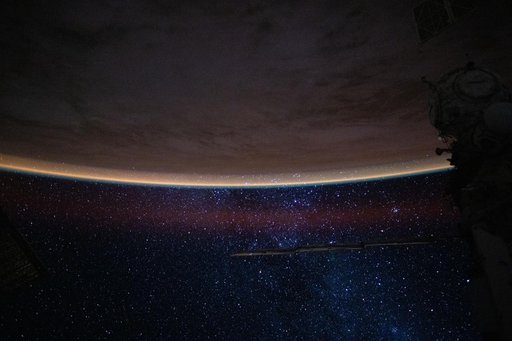 A bright orange airglow outlines Earth’s horizon beneath the starry expanse of the night sky