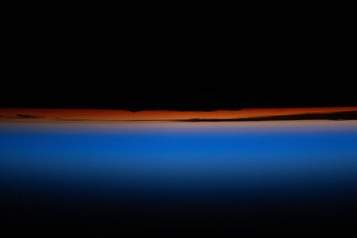 A multi-hued orbital sunset revealing the tops of clouds fades above Earth's horizon