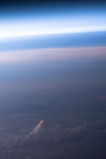An orbital sunset softens Earth’s atmosphere and cloud tops with light pink and blue hues