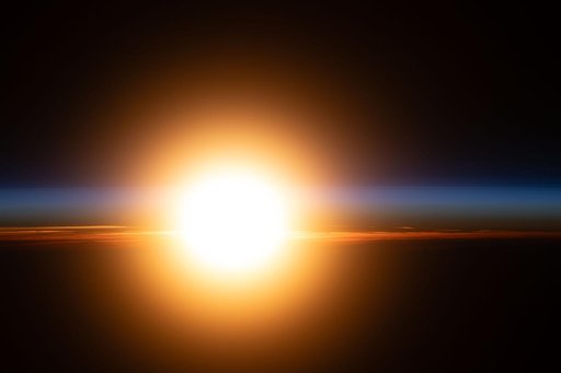 A bright orange sunburst illuminates Earth's atmosphere during an orbital sunrise