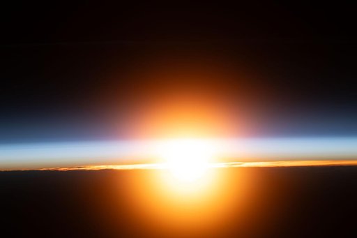 A bright orange sunburst illuminates Earth's atmosphere during an orbital sunrise