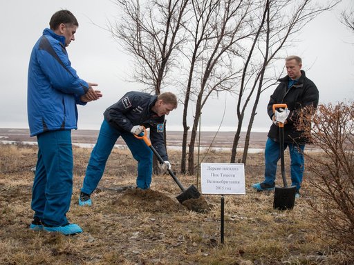 Behind the Cosmonaut Hotel crew quarters in Baikonur, Kazakhstan, Expedition 46-47 crewmember Tim Peake of the European Space Agency (center) plants a tree at a site bearing his name Dec. 9 in a traditional pre-launch ceremony. Looking on are his crewmates, Yuri Malenchenko of the Russian Federal Sp