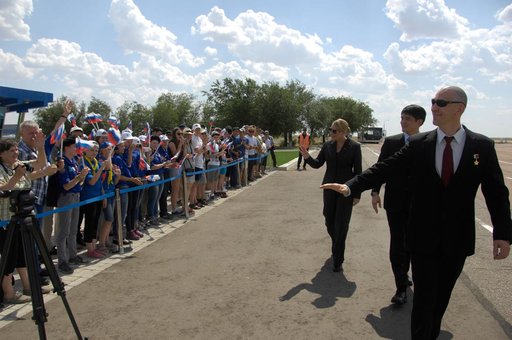 ISS Expedition 48-49 prime crewmembers Kate Rubins of NASA (left), Takuya Onishi of the Japan Aerospace Exploration Agency (center) and Anatoly Ivanishin of Roscosmos (right) wave to schoolchildren after arriving in Baikonur, Kazakhstan June 24 for final pre-launch training following a flight from S