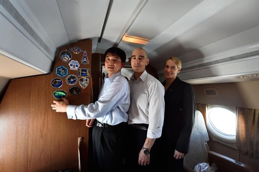 Aboard their aircraft on route to their launch site in Baikonur, Kazakhstan, ISS Expedition 48-49 crewmembers Takuya Onishi of the Japan Aerospace Exploration Agency (left), Anatoly Ivanishin of Roscosmos (center) and Kate Rubins of NASA (right) affix their mission insignia sticker to the wall June 