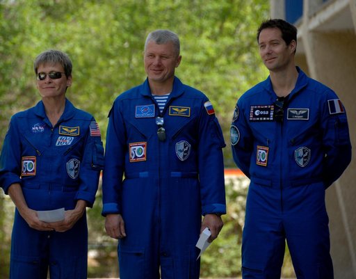 Outside their Cosmonaut Hotel crew quarters in Baikonur, Kazakhstan, Expedition 48-49 backup crewmembers Peggy Whitson of NASA (left), Oleg Novitskiy of Roscosmos (center) and Thomas Pesquet of the European Space Agency (right) listen to remarks June 26 during the traditional raising of the American