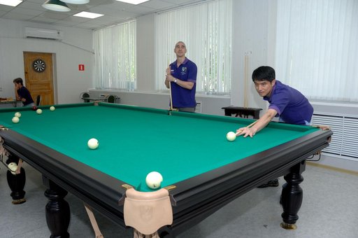At the Cosmonaut Hotel in Baikonur, Kazakhstan, Expedition 48-49 crewmember Takuya Onishi of the Japan Aerospace Exploration Agency (right) tries his hand at billiards June 30 during pre-launch activities as his crewmate, Anatoly Ivanishin of Roscosmos looks on. In the background on the left, backup