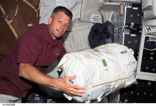 Swanson, STS-117 MS moves stowage bag on the MDDK of Space Shuttle Atlantis